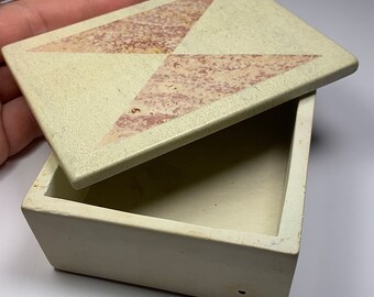 May include: A small, rectangular box made of light green stone with a lid. The lid has a geometric design of pink and white triangles.