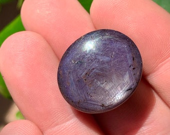 May include: A dark purple, round, polished gemstone with a swirling pattern of lighter purple and silver.