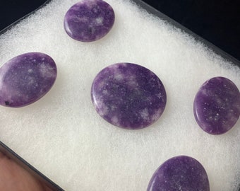 May include: Five smooth, oval-shaped stones with a purple and white marbled pattern. The stones are arranged in a white box with a black border.