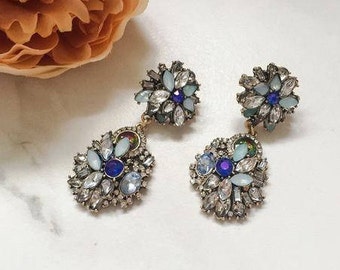 May include: A pair of dangle earrings with a floral design. The earrings are made of gold-toned metal and feature blue and white crystals.