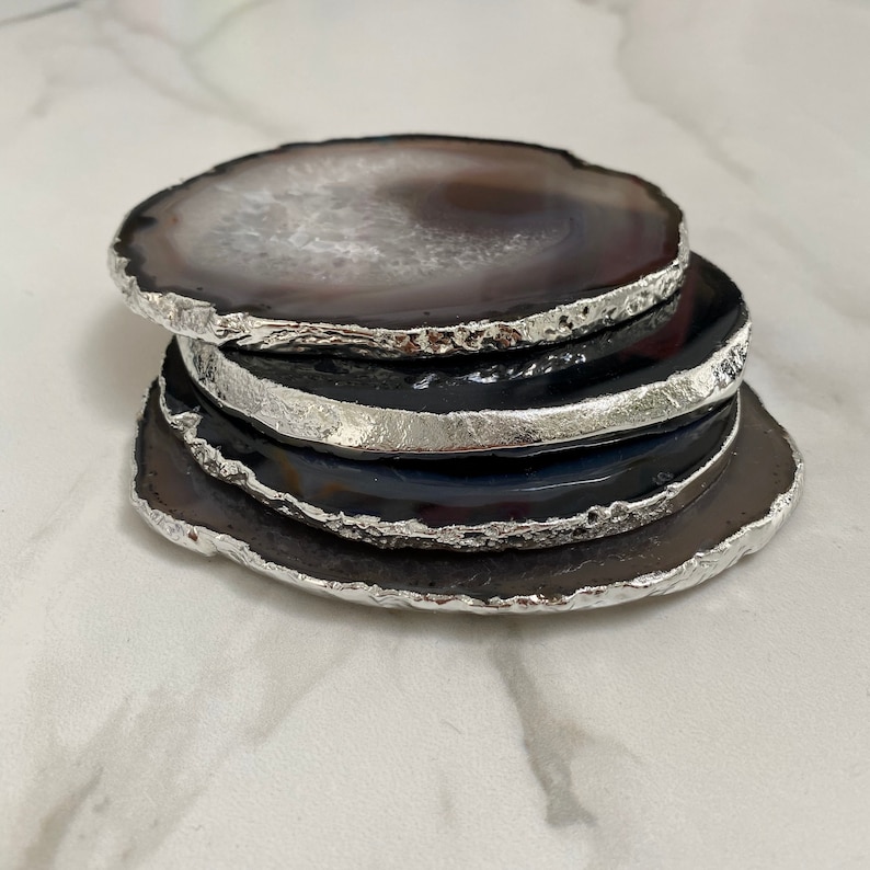 Peut inclure: Ensemble de quatre sous-verres en agate avec une bordure argent&eacute;e. Les sous-verres sont noirs et blancs avec un motif d'agate naturel.