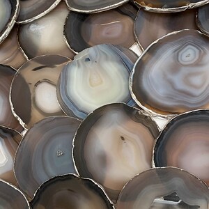 Peut inclure: Un ensemble de dessous-de-verre en agate avec une bordure argent&eacute;e. Les dessous-de-verre sont de diff&eacute;rentes nuances de brun et de gris avec des bandes blanches et brun clair.