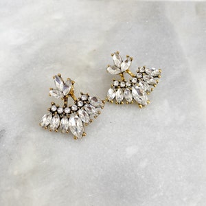 May include: A pair of gold tone earrings with clear crystal accents. The earrings are shaped like a fan and have a delicate, feminine design.