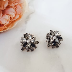 May include: A pair of silver tone earrings with black and clear rhinestones in a flower shape.
