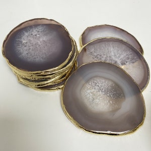 Peut inclure: Ensemble de six sous-verres en agate avec bordure dorée. Les sous-verres sont de couleur violet clair avec des motifs d'agate blancs.