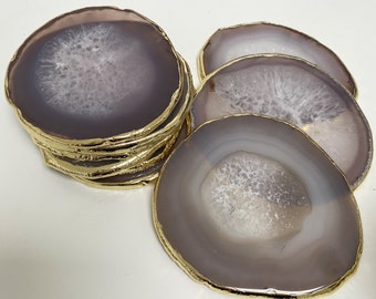 May include: Set of six agate coasters with gold trim. The coasters are a light purple color with white agate patterns.