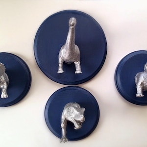 May include: Four silver dinosaur figurines mounted on blue circular wooden plaques. The dinosaurs are a triceratops, a stegosaurus, a brachiosaurus, and a tyrannosaurus rex.