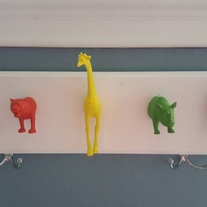 May include: A white wooden coat rack with five animal-shaped hooks. The hooks are a red lion, a red cat, a yellow giraffe, a green rhinoceros, and a blue gorilla.