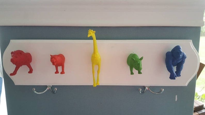 May include: A white wooden coat rack with five animal-shaped hooks. The hooks are a red lion, a red cat, a yellow giraffe, a green rhinoceros, and a blue gorilla.