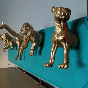May include: A teal blue wooden wall mounted coat rack with gold animal shaped hooks. The hooks are shaped like a lion, giraffe, gorilla, and a cheetah.