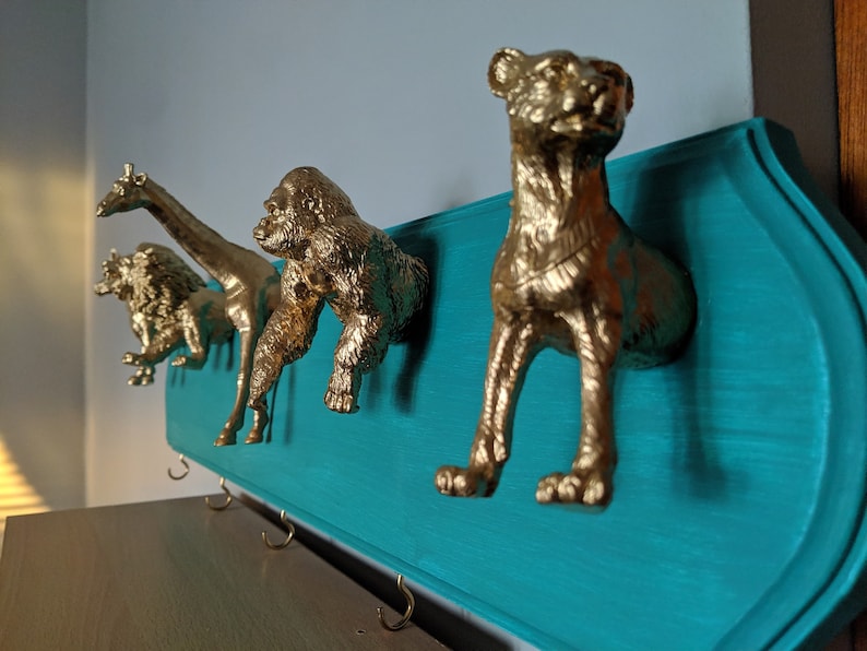 May include: A teal blue wooden wall mounted coat rack with gold animal shaped hooks. The hooks are shaped like a lion, giraffe, gorilla, and a cheetah.
