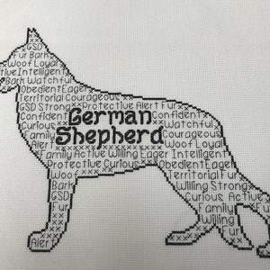 May include: Black and white cross-stitch design of a German Shepherd dog silhouette. The silhouette is filled with words describing the breed's traits, such as "loyal", "intelligent", "protective", and "curious".