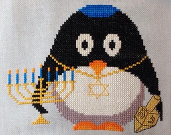 May include: A black and white penguin wearing a blue yarmulke and a gold necklace with a Star of David pendant. The penguin is holding a menorah with lit candles and a dreidel.