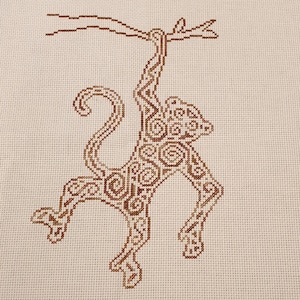 May include: A brown cross-stitch embroidery of a monkey hanging from a branch. The monkey is detailed with intricate patterns and swirls.