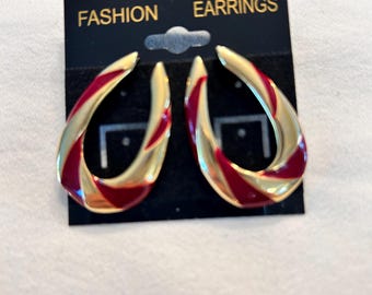 May include: Gold-tone earrings with a teardrop shape and red enamel accents. The earrings are displayed on a black card that reads "FASHION EARRINGS". The earrings have a glossy finish and a modern design.