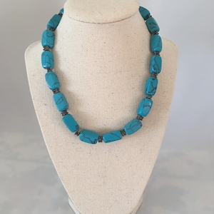 Könnte beinhalten: Eine türkisblaue Halskette mit rechteckigen Perlen und silbernen Akzenten. Die Halskette wird auf einer weißen Mannequin-Büste präsentiert.