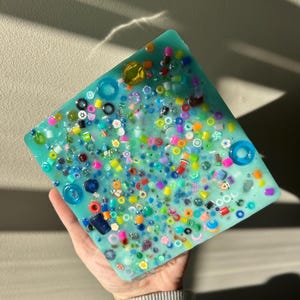 May include: A square turquoise resin tray with a variety of colorful beads and small trinkets embedded in the surface.