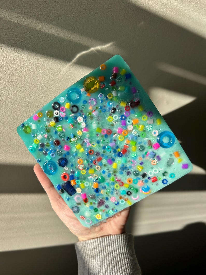 May include: A square turquoise resin tray with a variety of colorful beads and small trinkets embedded in the surface.