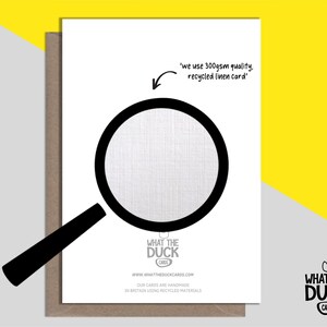 Peut inclure: Une carte blanche avec une illustration de loupe noire. Le texte "we use 300gsm quality, recycled linen card" est &eacute;crit sur la carte. Le texte "WHAT THE DUCK CARDS" est &eacute;crit en noir sur fond blanc avec une illustration de canard en caoutchouc jaune.