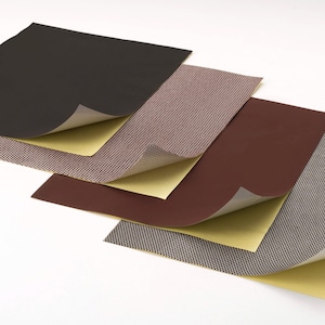 Puede incluir: Cuatro hojas de papel de lija con diferentes texturas y colores. Las hojas están apiladas una encima de la otra, con la hoja superior parcialmente despegada para revelar el respaldo adhesivo.