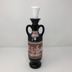 May include: A black glass decanter with a white stopper. The decanter is decorated with a red and white design of a Greek scene. The label reads "Since 1795 Beam".