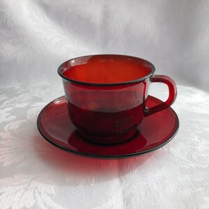 May include: A red glass teacup and saucer set. The cup and saucer are both a deep, rich red color and have a glossy finish.