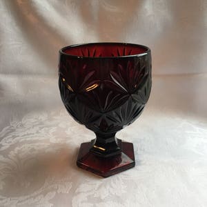 May include: A deep red glass bowl with a cut glass design sits on a pedestal base. The bowl is made of heavy glass and has a vintage look.