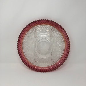 May include: A clear glass serving dish with four sections, featuring a raised diamond pattern. The dish has a deep burgundy rim with a diamond pattern.