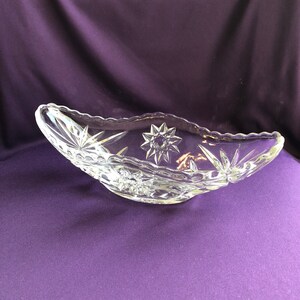 May include: A clear glass bowl with a scalloped edge and a starburst pattern. The bowl is on a purple background.