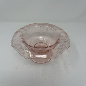 May include: A pink glass bowl with a scalloped edge and a delicate etched floral design. The bowl is on a pedestal base.