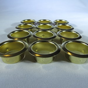 May include: A set of 12 gold-colored metal grommets, arranged in a staggered pattern on a white surface.