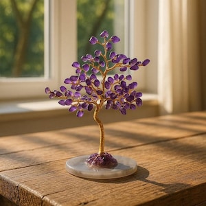 Könnte beinhalten: Eine dekorative Baumskulptur mit goldfarbenem Stamm und Ästen, verziert mit lila Amethystblättern. Der Baum steht auf einem runden, hellfarbenen Sockel und wird auf einer Holzoberfläche präsentiert. Die Skulptur befindet sich in der Nähe eines Fensters.
