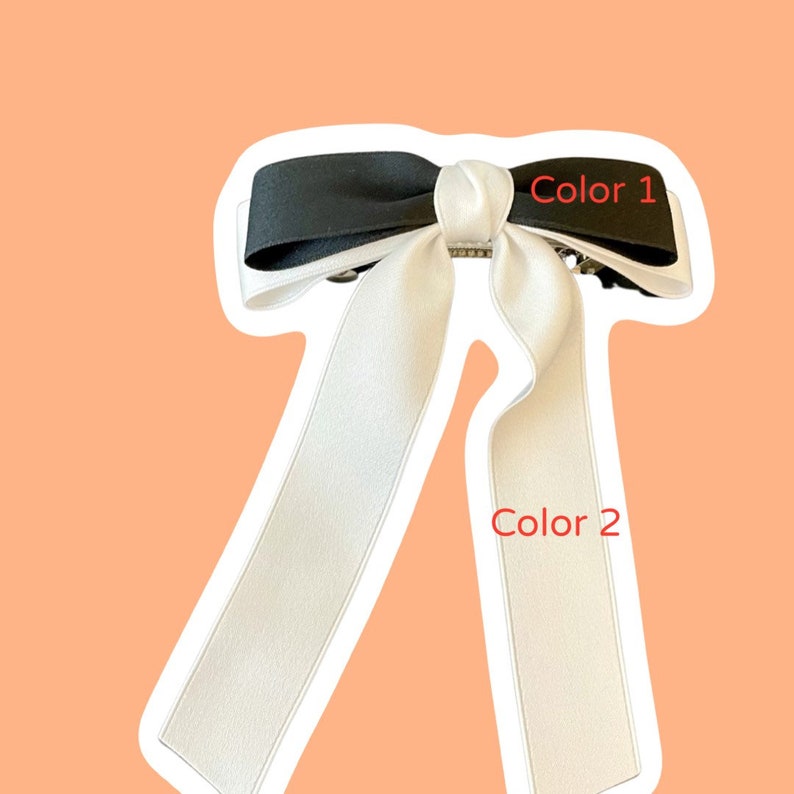 Pode incluir: Um la&ccedil;o de cabelo preto e branco com um la&ccedil;o grande no topo e duas caudas longas. O la&ccedil;o est&aacute; etiquetado como "Cor 1" e as caudas est&atilde;o etiquetadas como "Cor 2".