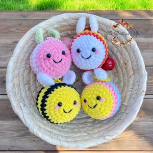May include: Four crocheted stuffed toys in a woven basket. The toys are a pink ladybug, a white bunny, a yellow and black bee, and a yellow, pink, and blue bee. Each toy has a smiling face.