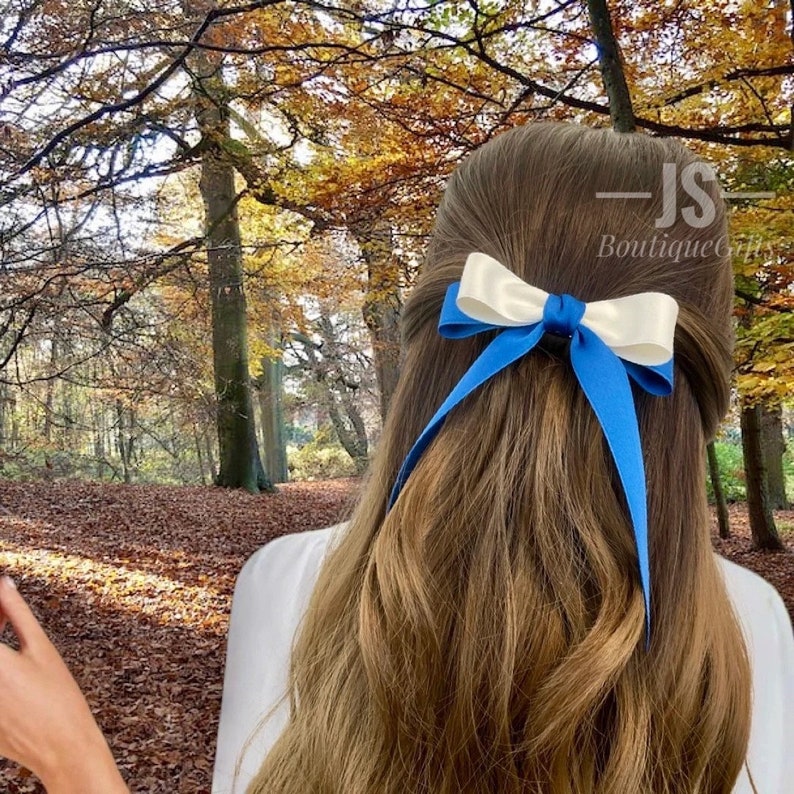 Pode incluir: Um prendedor de cabelo de fita de cetim azul e branco. O la&ccedil;o &eacute; amarrado com uma fita azul e uma fita branca. O prendedor de cabelo &eacute; usado no cabelo de uma mulher.