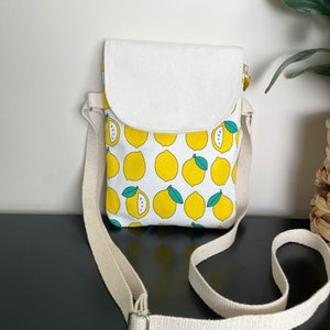May include: A small white canvas crossbody bag with a lemon print. The bag has a flap closure and an adjustable strap.