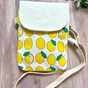 May include: A white canvas crossbody bag with a lemon print. The bag has a flap closure and a long adjustable strap.