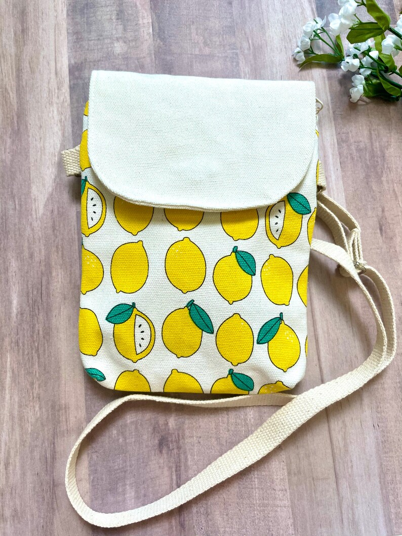 May include: A white canvas crossbody bag with a lemon print. The bag has a flap closure and a long adjustable strap.
