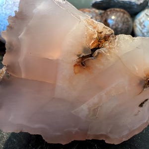 May include: A large, translucent pink agate with brown and white inclusions. The agate has a rough, natural texture and is a beautiful example of this type of gemstone.