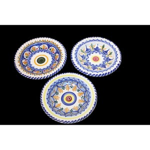 Puede incluir: Tres platos decorativos de cerámica con intrincados diseños pintados a mano. Cada plato presenta una base blanca con un patrón floral azul, amarillo y verde. Los platos están dispuestos sobre un fondo negro.