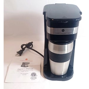 Op de afbeelding: Een zwart koffiezetapparaat voor één kopje met een zilveren band en het Cook's Essentials-logo. Het bevat een bijpassende roestvrijstalen reisbeker met een zwarte grip en een gedrukte handleiding met het modelnummer CM-111 zichtbaar.