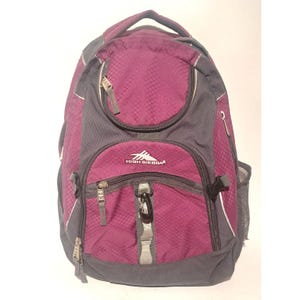 May include: A High Sierra backpack in a combination of burgundy and gray. The backpack features multiple zippered compartments, a mesh side pocket, and a top handle. The High Sierra logo is visible on the front pocket. The backpack has a diamond pattern.