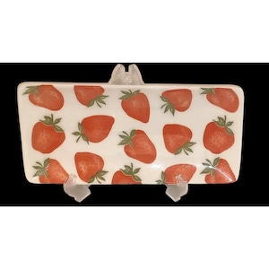 May include: Rectangular white ceramic serving dish decorated with red strawberries and green leaves. The dish is supported by clear plastic stands. The strawberries are evenly spaced across the surface of the dish.