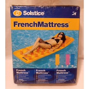 Może przedstawiać: Pudełko na nadmuchiwany materac do pływania Solstice French Mattress. Pudełko jest niebiesko-żółte ze słowami "French Mattress". Obraz przedstawia kobietę w czarnym bikini leżącą na pomarańczowym materacu w basenie.