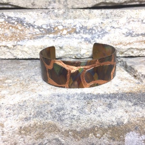 Puede incluir: Un brazalete de cobre con un patrón irregular único. El brazalete tiene una base marrón oscuro con contornos y acentos de color cobre. El diseño abierto permite un uso fácil. El brazalete mide aproximadamente 3,8 cm de ancho.