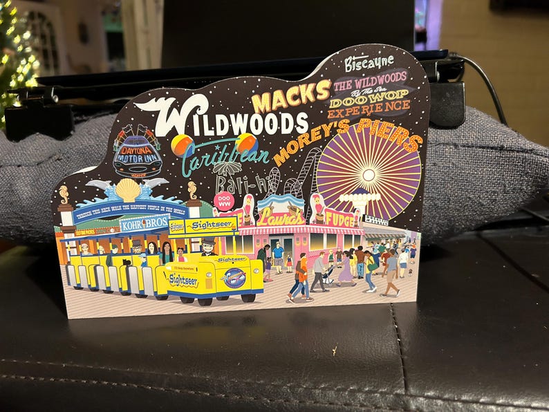 May include: A colorful illustration of a boardwalk amusement park with a Ferris wheel, shops, and a yellow and blue sightseeing train. The text "Wildwoods" is featured in the illustration.