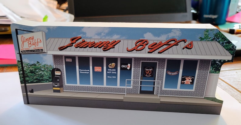 May include: A model of a red and white storefront with the words "Jimmy Buff's" in red lettering. The storefront has several windows with signs that say "Open", "Italian Hot Dogs", and "Throwback Thursdays".