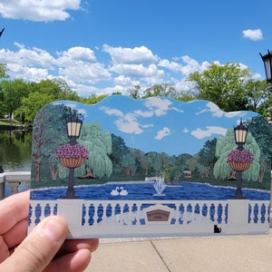 May include: A hand holds a colorful illustration of a park scene with a pond, trees, and a fountain. The illustration is titled "Hawthorne Hill Park".