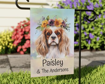 May include: A personalized garden flag with a watercolor illustration of a Cavalier King Charles Spaniel wearing a flower crown. The text on the flag reads "Paisley & The Andersons".