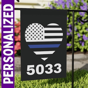 May include: Black garden flag featuring a heart-shaped design with the American flag and a blue line. The number "5033" is printed below the heart. The word "PERSONALIZED" is printed vertically on the left side.